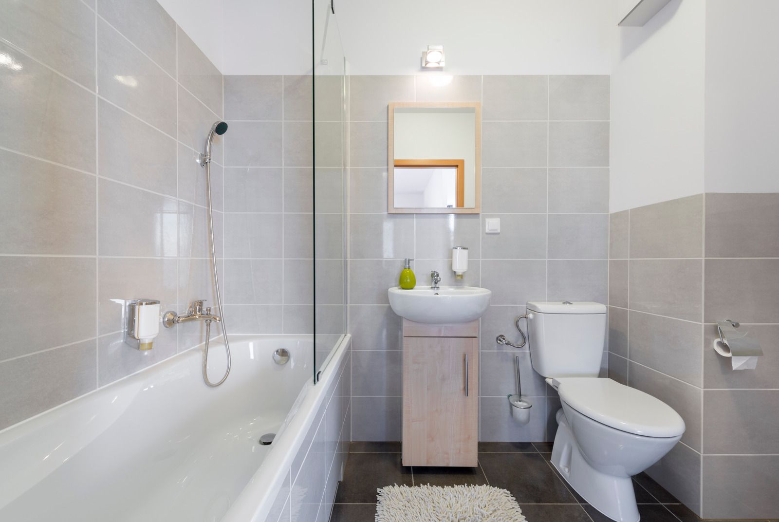Nyt badeværelse med lysegrå vægfliser, badekar med bruser, håndvask og toilet